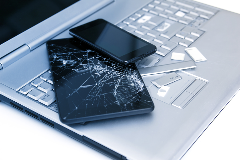 Close up of broken phone and tablet resting on a silver partially broken laptop, before the user learns how to get photos and other files from broken devices.